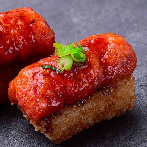 Close-up of a Temakase Hand Roll Bar sushi piece with red sauce and green onions.
