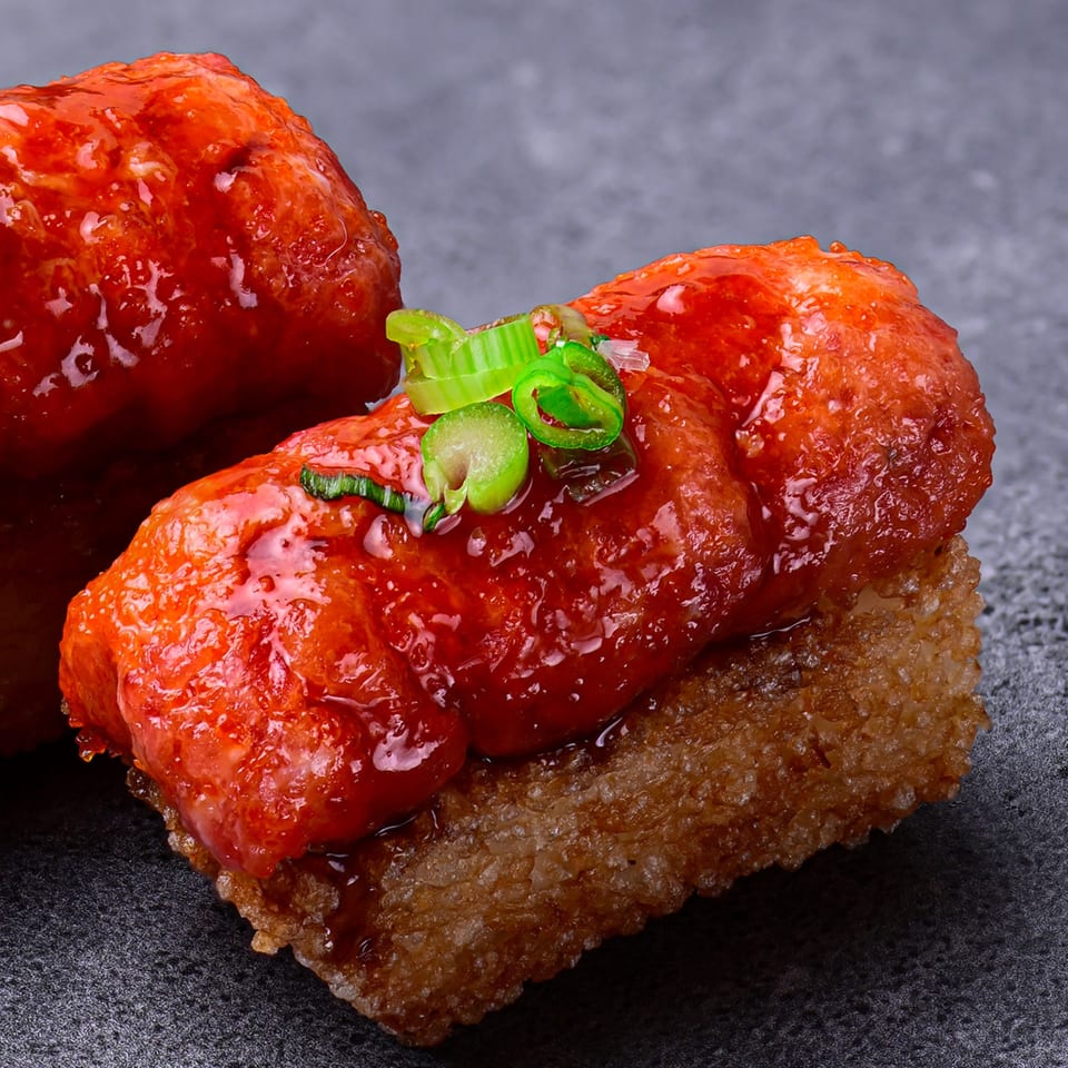 Close-up of a Temakase Hand Roll Bar sushi piece with red sauce and green onions.