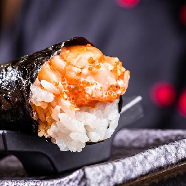 Close-up of a Temakase hand roll, filled with rice, salmon, and bright orange roe.
