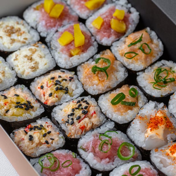 A close-up of a variety of Temakase hand rolls in a box, featuring different toppings and fillings.
