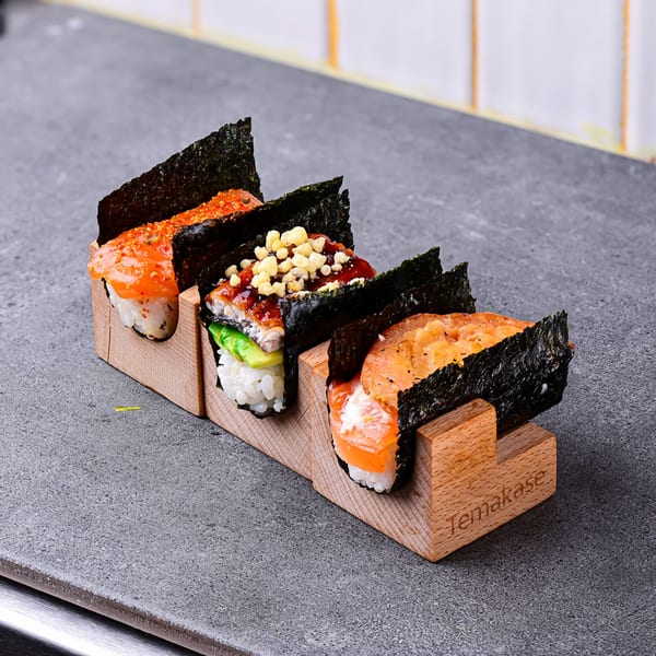 Three Temakase hand rolls with salmon, eel, and roe fillings, served in a wooden holder.