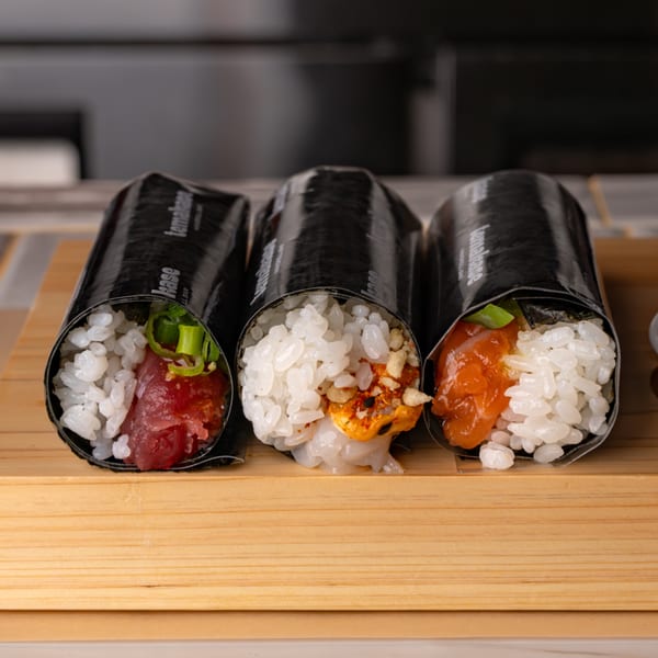 Three Temakase hand rolls on a wooden board, filled with tuna, scallop, and salmon.