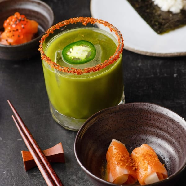 Temakase Hand Roll Bar's green cocktail with a chili-salted rim, sushi, and chopsticks.