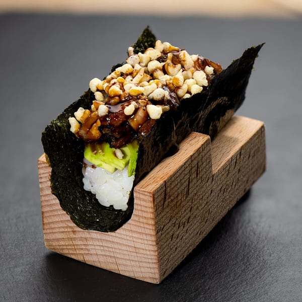 Temakase hand roll with rice, avocado, and toppings, served in a wooden holder.