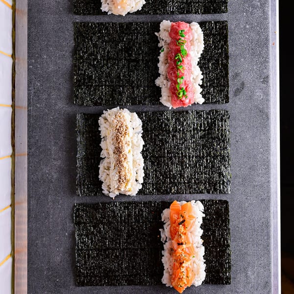 Four Temakase hand rolls with various fillings like salmon, tuna, and crab, on nori sheets.