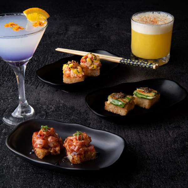 Assortment of Temakase sushi appetizers and two cocktails on a dark textured surface.
