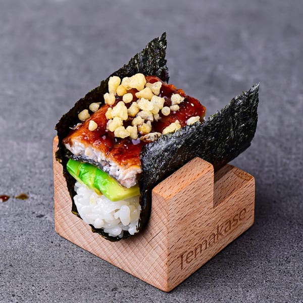Temakase hand roll with eel, avocado, and crispy toppings, served in a wooden holder.