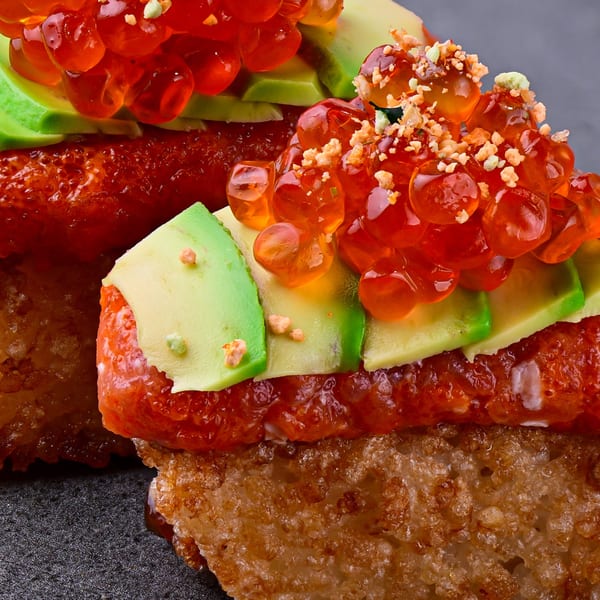 Close-up of Temakase sushi with bright red roe, avocado slices, and crispy rice.