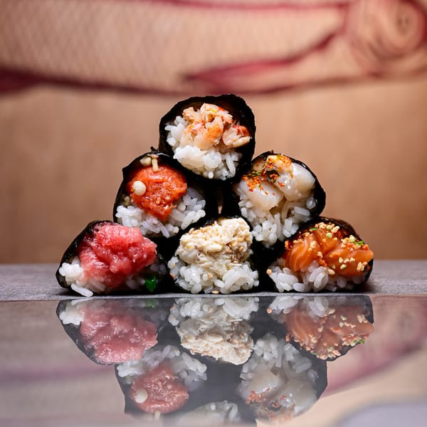 A pyramid of six Temakase hand rolls with various fillings, reflected on a shiny surface.