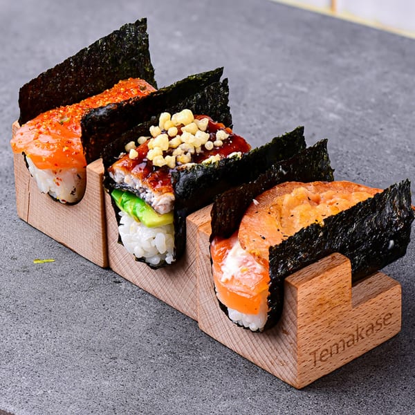 Three Temakase hand rolls with salmon, eel, and seared salmon, presented in a wooden holder.