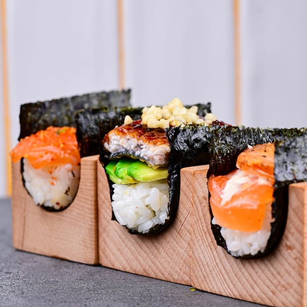 Three Temakase hand rolls in wooden holders, featuring salmon, eel with avocado, and another salmon roll.