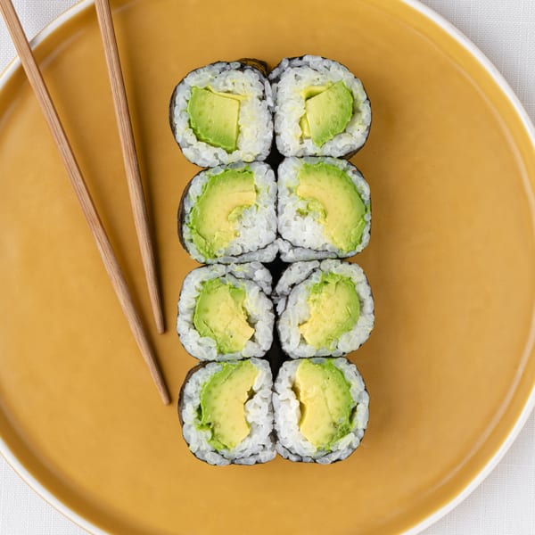 Six avocado sushi rolls and chopsticks on a mustard yellow plate, from Temakase Hand Roll Bar.