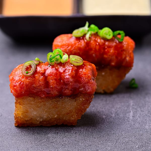 Two pieces of Temakase crispy rice sushi topped with spicy tuna and green onions.