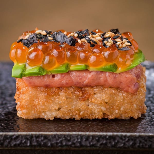 Crispy rice sushi with tuna, avocado, salmon roe, seaweed, and sesame seeds on a dark plate.
