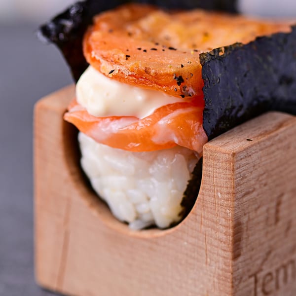 A Temakase hand roll with rice, salmon, mayonnaise, and a fried topping, served in a wooden holder.