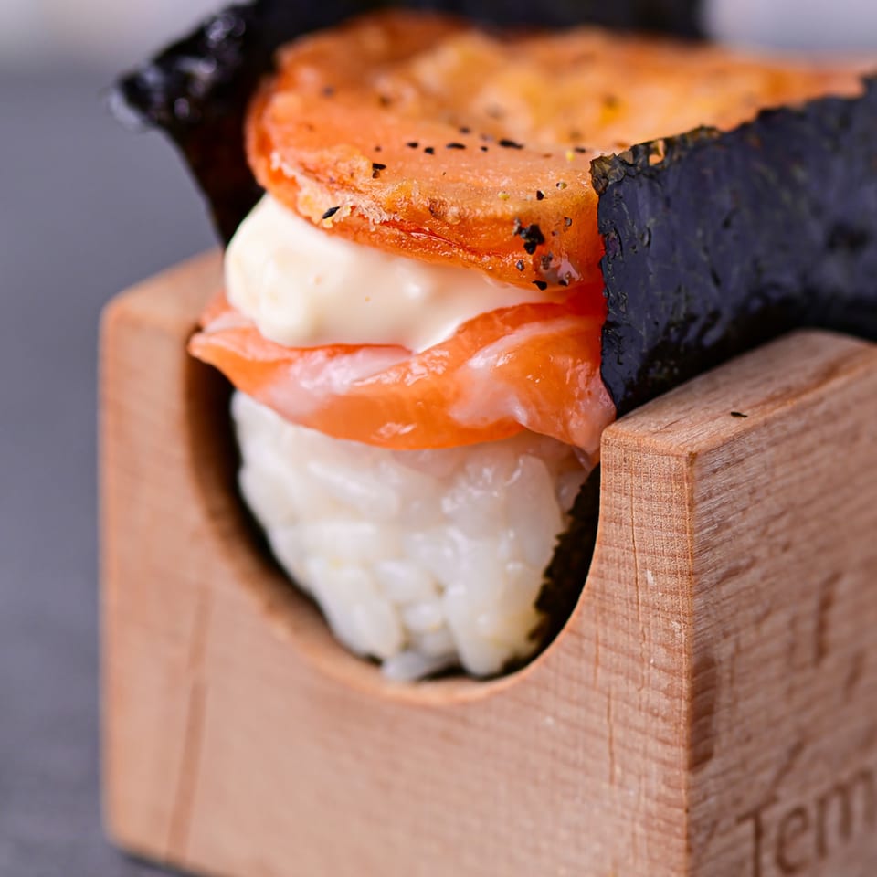 A Temakase hand roll with rice, salmon, mayonnaise, and a fried topping, served in a wooden holder.