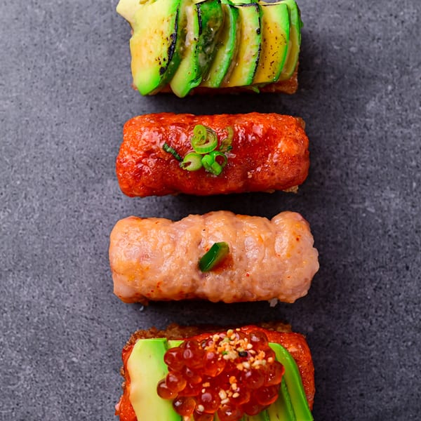 Four Temakase sushi pieces with avocado, salmon, and roe on a dark grey surface.