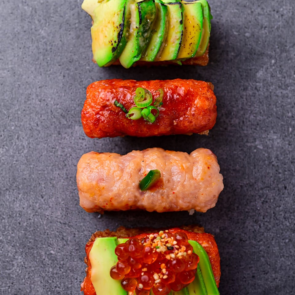 Four Temakase sushi pieces with avocado, salmon, and roe on a dark grey surface.