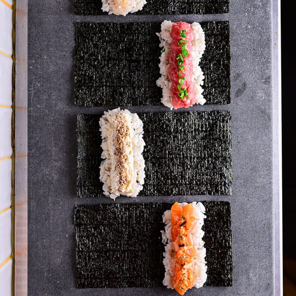 Overhead view of various Temakase hand rolls with rice and different toppings on nori sheets.