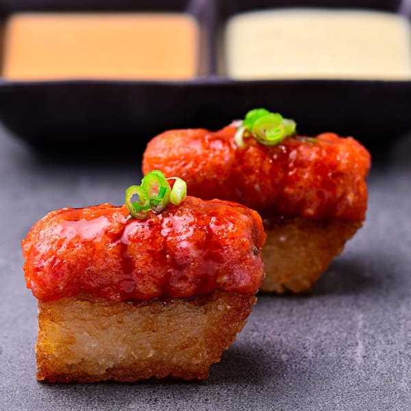 Two pieces of crispy rice sushi topped with red spicy tuna and green scallions.